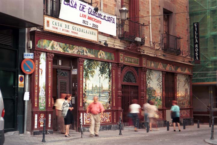 Madrid: Casa De Guadalajara and Villa Rosa. Storefronts on a sidewalk with pedestrians walking about. (80K)